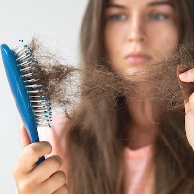 Frau betrachtet ausgefallene Haare in einer Bürste, symbolisch für Haarausfall und medizinische Labordiagnostik zur Analyse von Hormonstatus, Nährstoffmangel und genetischen Ursachen in der Laborambulanz.